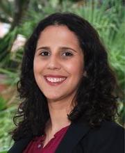 headshot photo of Dr. Rachel Navarre smiling with long dark brown curly hair, wearing a black blazer over a maroon button down top