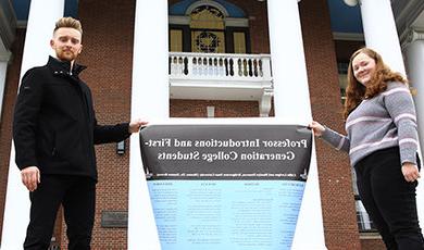 学生们在博伊登大厅的柱子前举着一张他们研究的海报